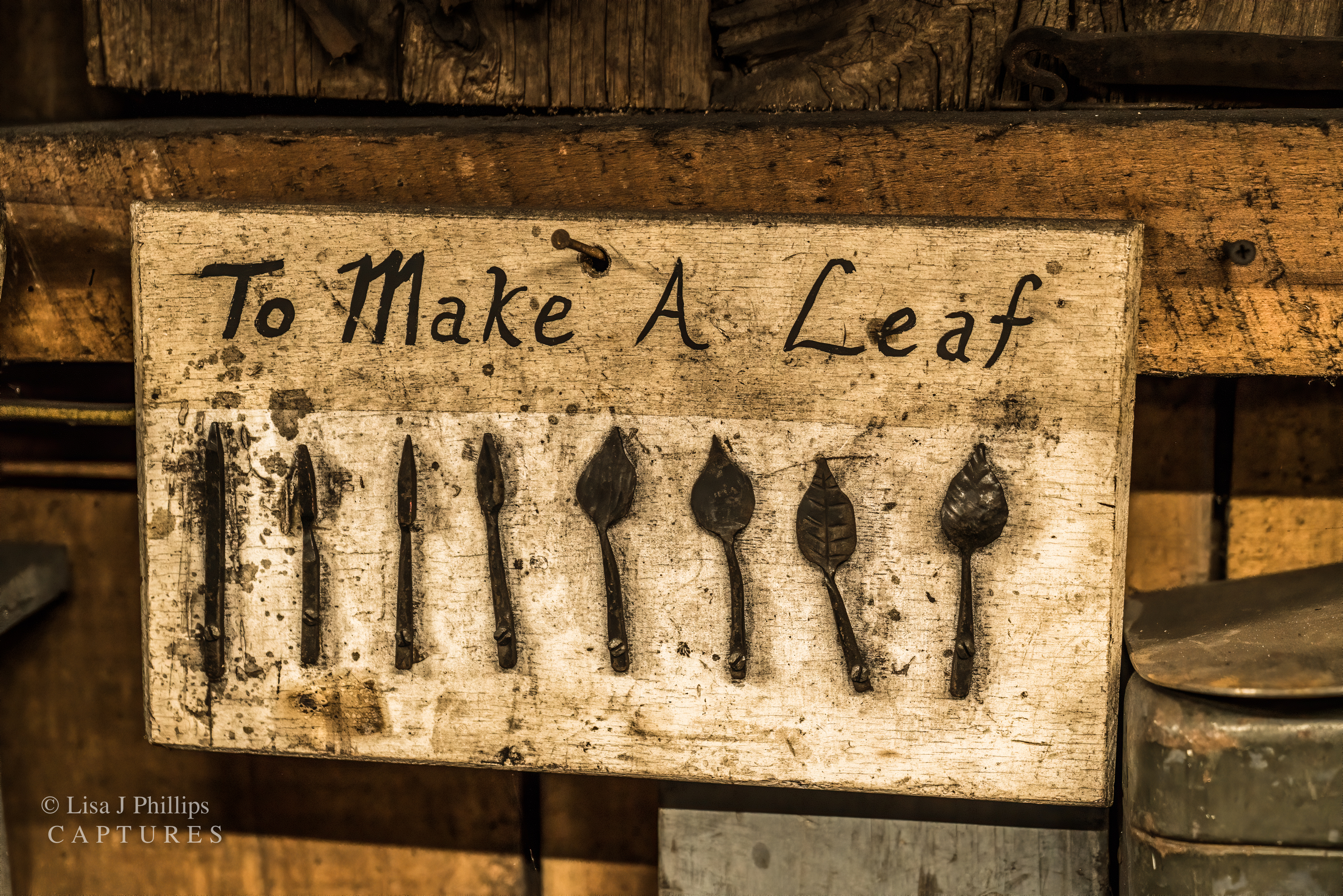 A wooden board nailed to a wall. It reads &lsquo;To Make A Leaf&rsquo; across the top. Below are eight pieces of steel showing each of the steps to forging a leaf,